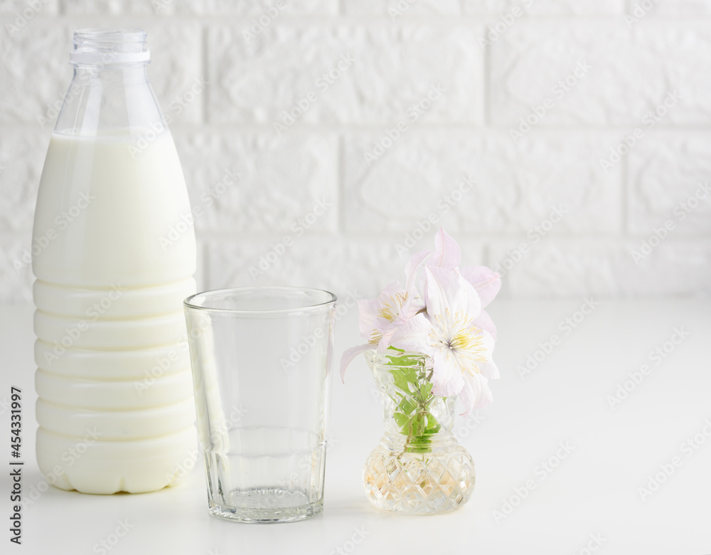 plastic bottle with milk and empty glass cup on a white table. Breakfast plastic bottle with milk and empty glass cup on a white table. Breakfast