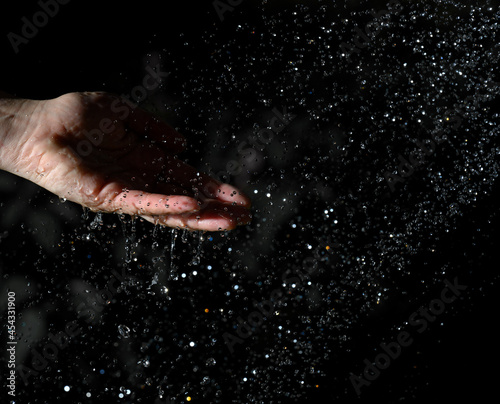 female hand and flying drops of water on a black background