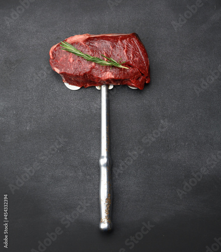  raw piece of beef steak lie on an iron knife, black background