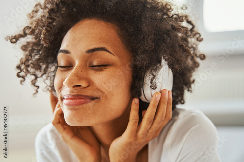 Smiling pleased dark-haired female wearing wireless headphones
