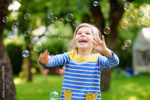 Happy little blonde preschool girl having fun with blowing soap bubble blower. Cute child playing on sunny summer day. Happy active funny healthy kid. Activity for children.