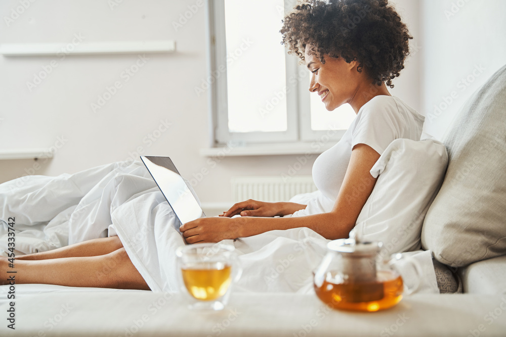 Smiling lady working on her portable personal computer in the bedroom