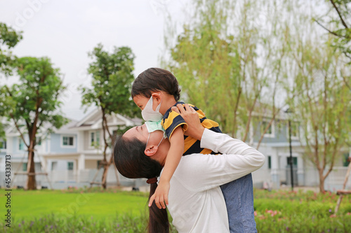 Asian mom carrying her son with wearing protective face mask and kissing in public garden during coronavirus and flu outbreak