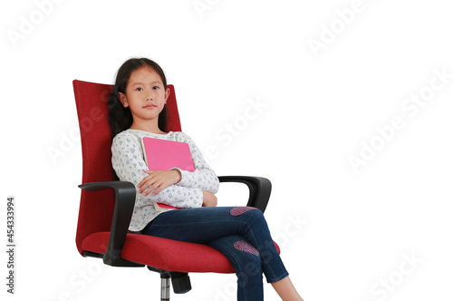 Asian young girl kid hugging a book sitting on red fabric chair isolated on white background. Image in studio with Clipping path