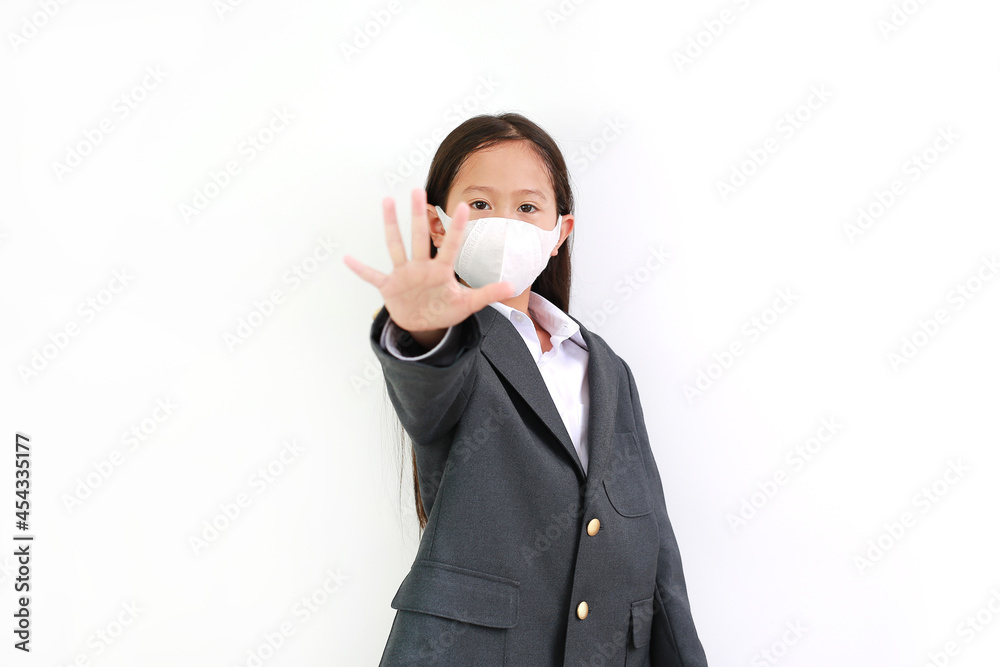 Asian little girl child wearing formalwear shirt, student suit and protective face mask showing hand stop sign on white background Asian little girl child wearing formalwear shirt, student suit and protective face mask showing hand stop sign on white background