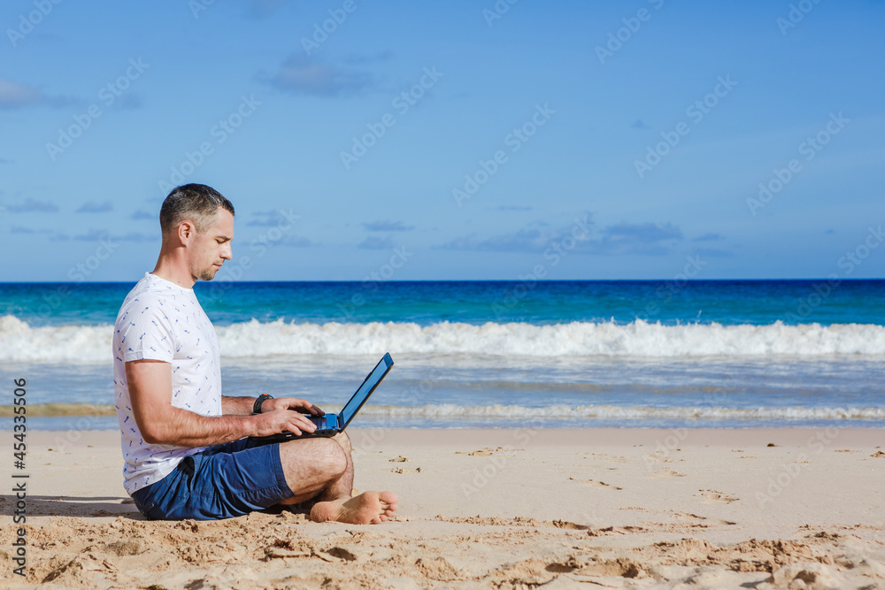 Young man with laptop working on the sand beach