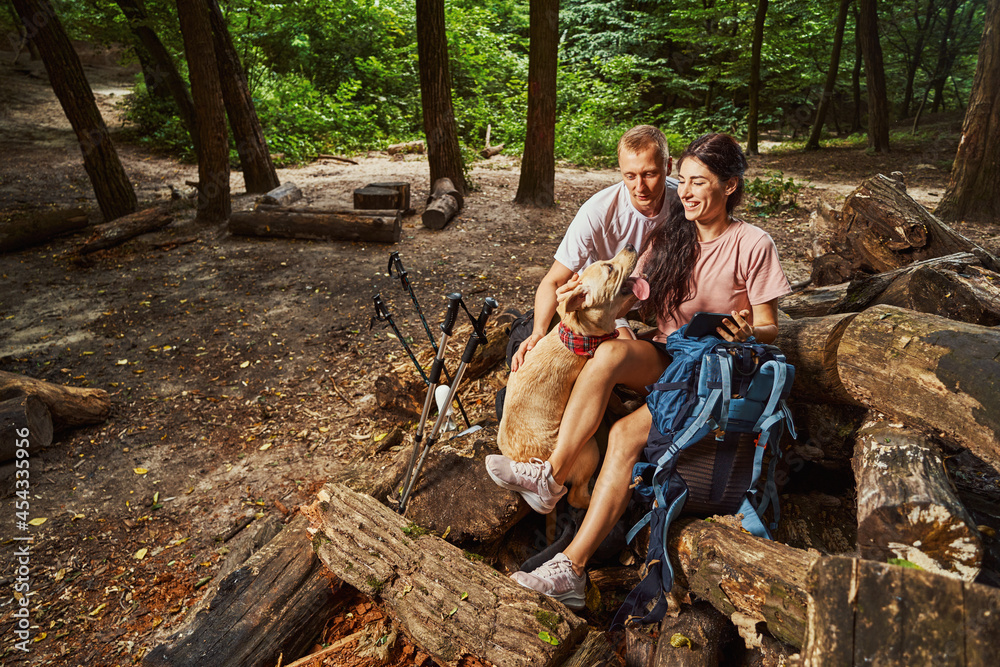 Cheerful couple with dog and smartphone in forest