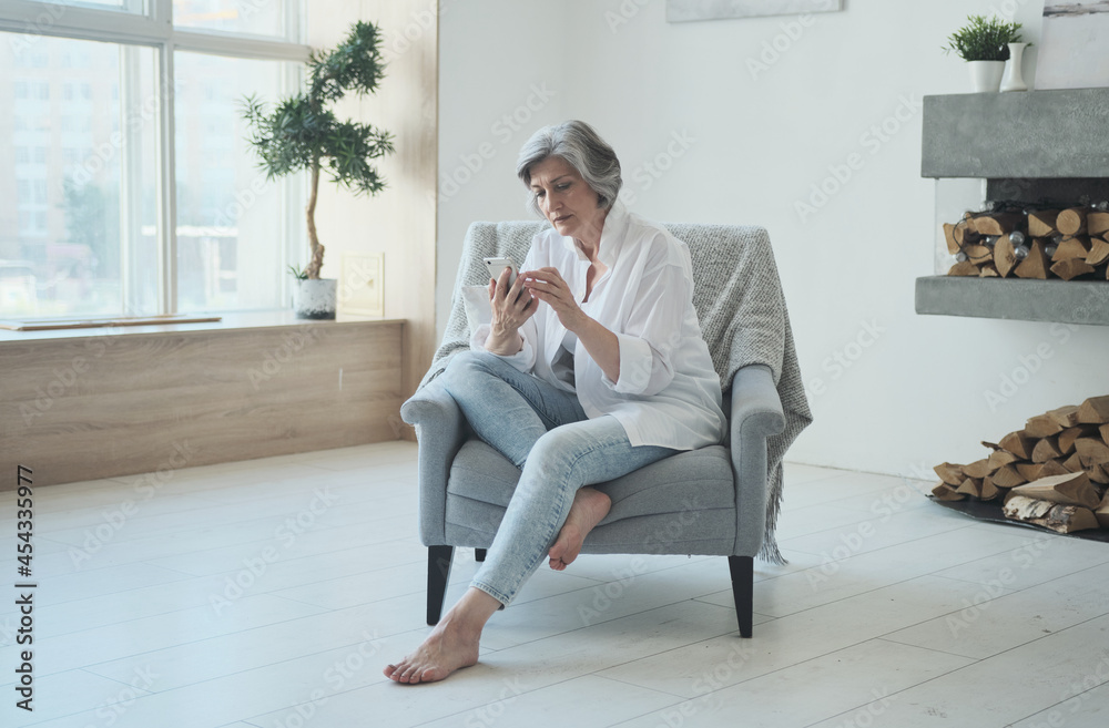 Relaxed mature old woman using mobile phone applications communicating in social network or shopping online, smartphone scrolling social media swiping scrolling, old businesswoman enjoying success