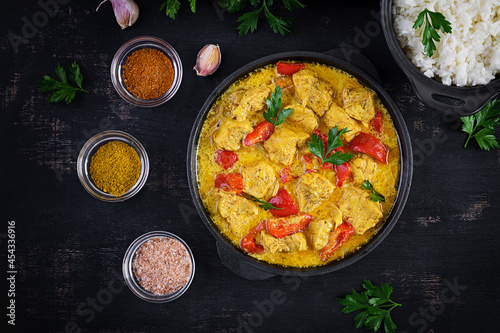 Traditional Indian curry chicken masala. Indian chicken curry with sweet peppers and rice in bowl, spices, dark background. Traditional Indian dish. Top view, flat lay