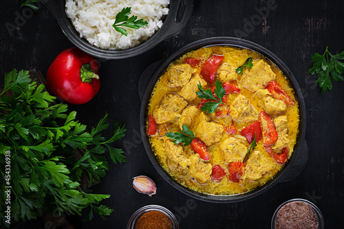 Traditional Indian curry chicken masala. Indian chicken curry with sweet peppers and rice in bowl, spices, dark background. Traditional Indian dish. Top view, flat lay