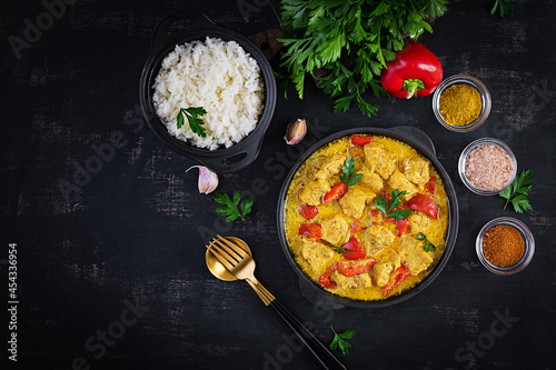 Traditional Indian curry chicken masala. Indian chicken curry with sweet peppers and  rice in bowl, spices, dark background. Traditional Indian dish. Top view, flat lay