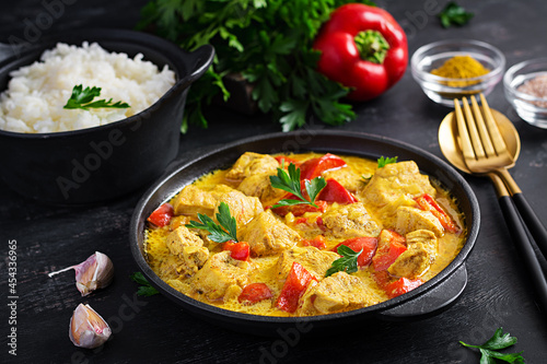 Traditional Indian curry chicken masala. Indian chicken curry with sweet peppers and rice in bowl, spices, dark background. Traditional Indian dish.