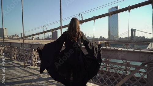 Woman in black long flowing dress walks across the Brooklyn Bridge in New York.