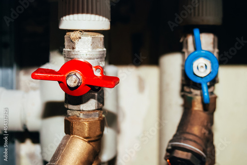 Two valves on plastic and metal pipes with hot and cold water. Open blue and closed red switches. Hot water is turned off