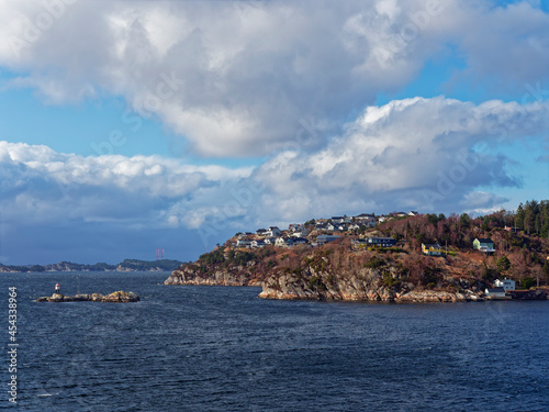Traditional Norwegian Houses on a rocky Headland in the Fjord with a Navigation Marker just outside Bergen on a sunny day in April.