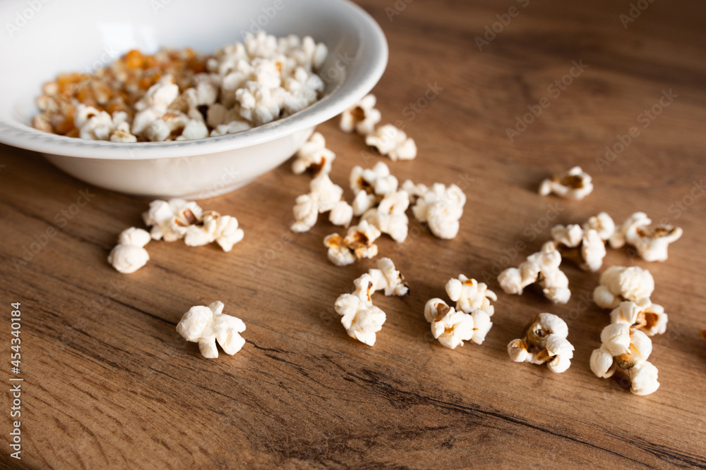 white plate with corn grains and sprinkled popcorn on a wooden table white plate with corn grains and sprinkled popcorn on a wooden table