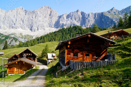 hiking trail leading through scenic alpine village Neustatt Alm or Neustatt valley with rustic alpine cabins by the foot of Dachstein mountain in Steiermark or Styria in the Austrian Alps (Austria)