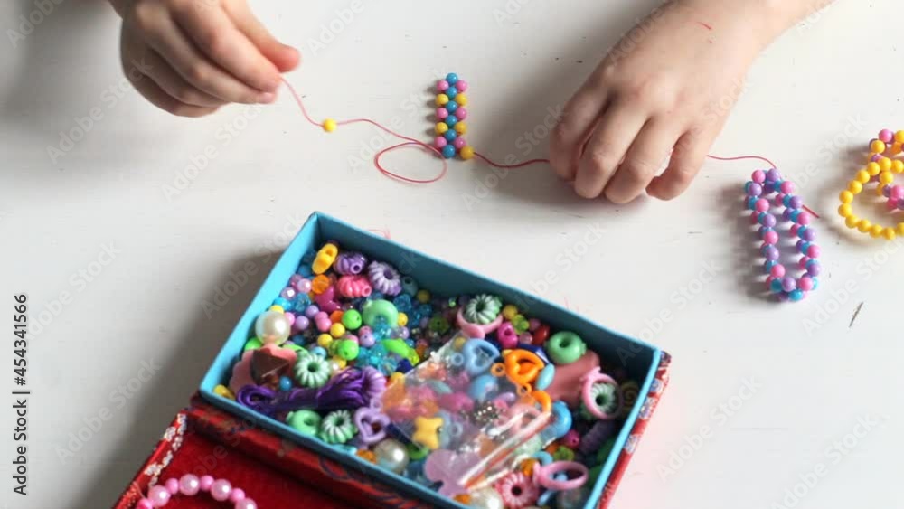 A little girl is stringing beads on a string to create a bracelet A little girl is stringing beads on a string to create a bracelet