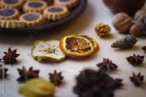 Fall season photo. Dried slices of orange, apple, acorns, physalis, and in the background there is a plate of cookies