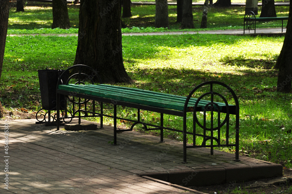 Beautiful bench in the city park. Bench against the backdrop of park trees and green grass. Beautiful bench in the city park. Bench against the backdrop of park trees and green grass.