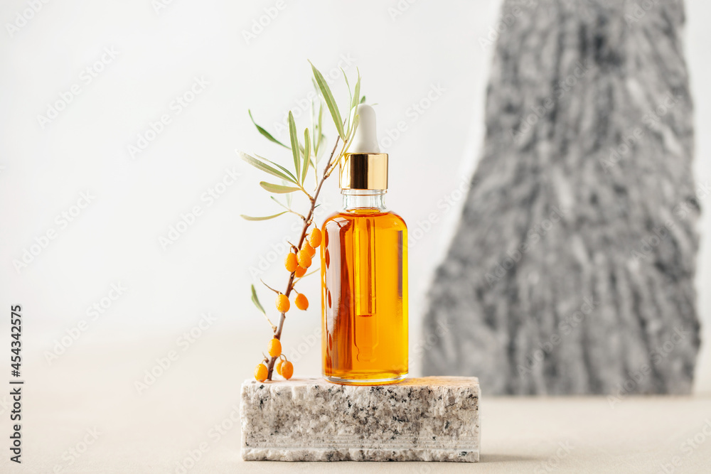 Essential oil and branch of sea-buckthorn with berries and leaves on stone podium. Natural cosmetic Essential oil and branch of sea-buckthorn with berries and leaves on stone podium. Natural cosmetic