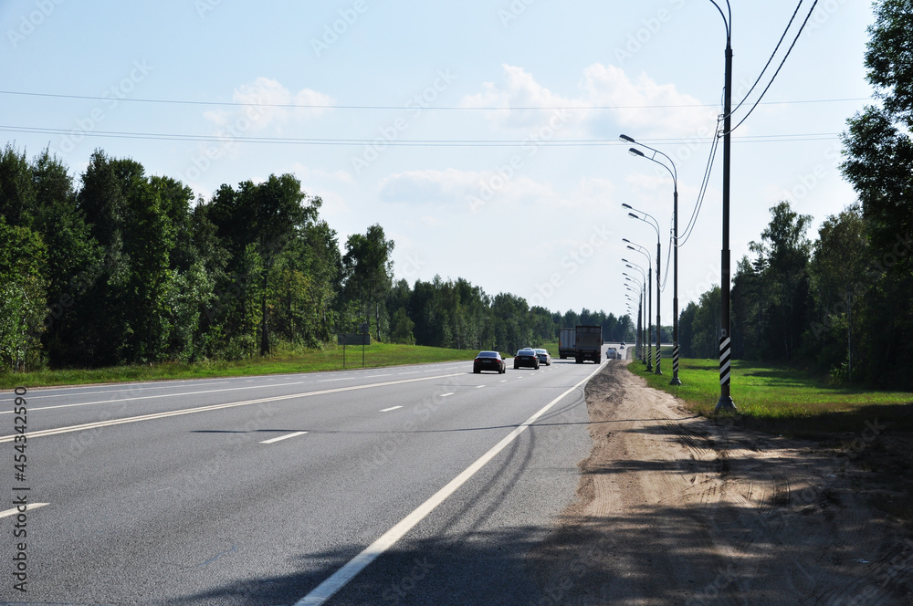 Panorama of the road on a summer day. Several cars and trucks are driving along the road.