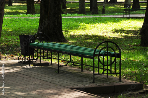 Beautiful bench in the city park. Bench against the backdrop of park trees and green grass.