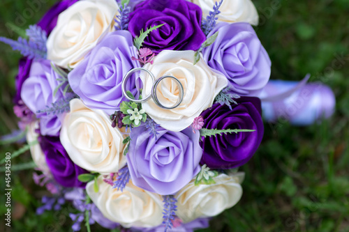 Wedding bouquet of satin roses and gold rings. Artificial or fake pink  violet and purple rose in bridal flower.