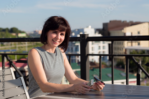 A happy positive brunette on the street in a cafe at a table is waiting for her order.