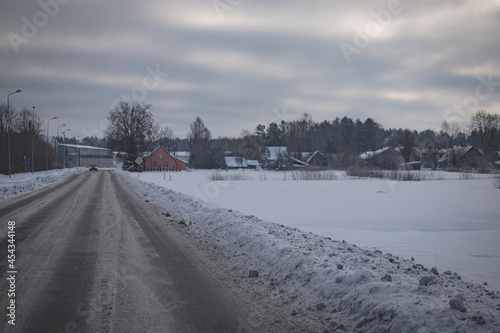 slippery dirty asphalt road through Latvia village in cold winter morning. Snow covered road on right side © Neils