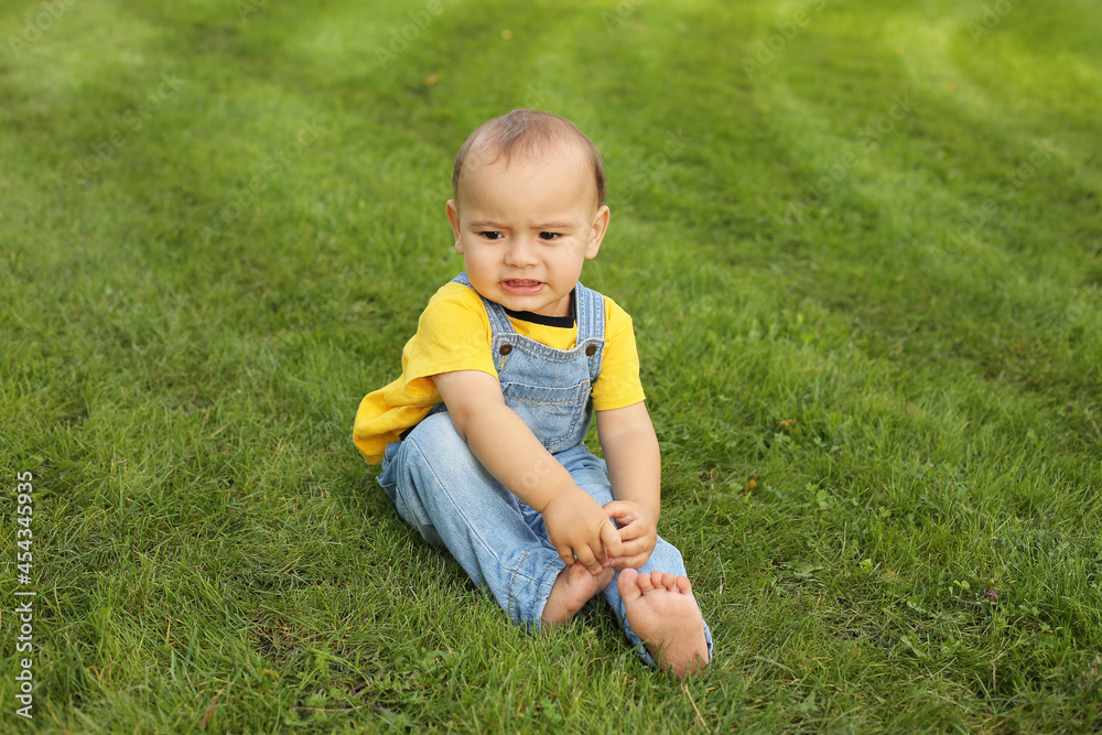 a beautiful little boy in a yellow T-shirt and a denim suit is sitting on the lawn in the park
a beautiful little boy in a yellow T-shirt and a denim suit is sitting on the lawn in the park