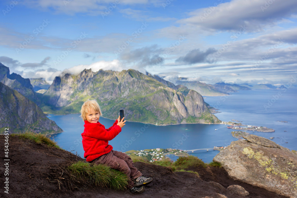 Fototapeta premium Cute child, standing on top of the mountains and looking down on Reine after climbing Reinebringen treeking path with lots of stairs