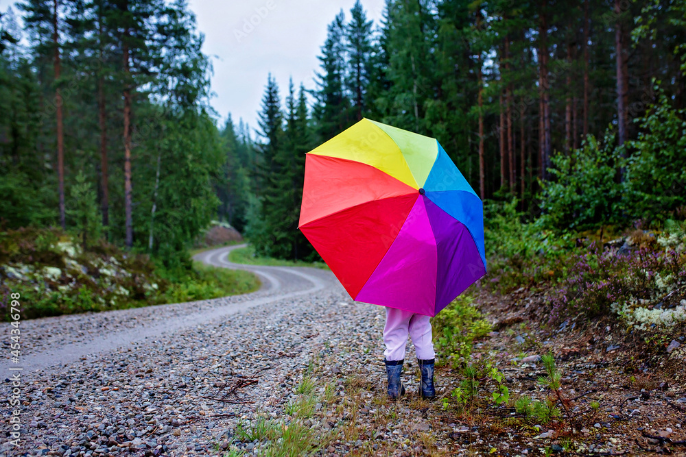 Cute toddler child with colorful umbrella, playing in the forest on a rainy day