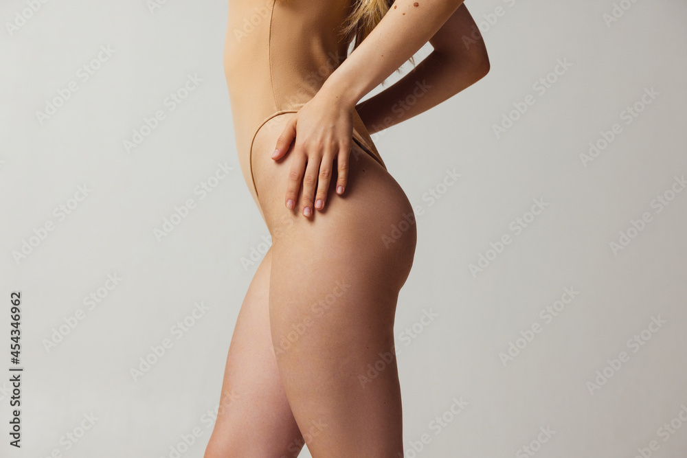 Side view of slender female legs with well-kept skin and some birthmarks isolated over light studio background. Natural beauty, wellness, healthy lifestyle concept.