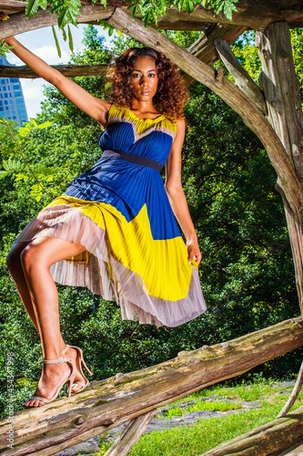 Obraz na płótnie Woman Playing in Park. Dressing in a sleeveless, yellow and blue pattern dress, a young pretty black girl with long curly hair is dancing around like a butterfly. . w salonie