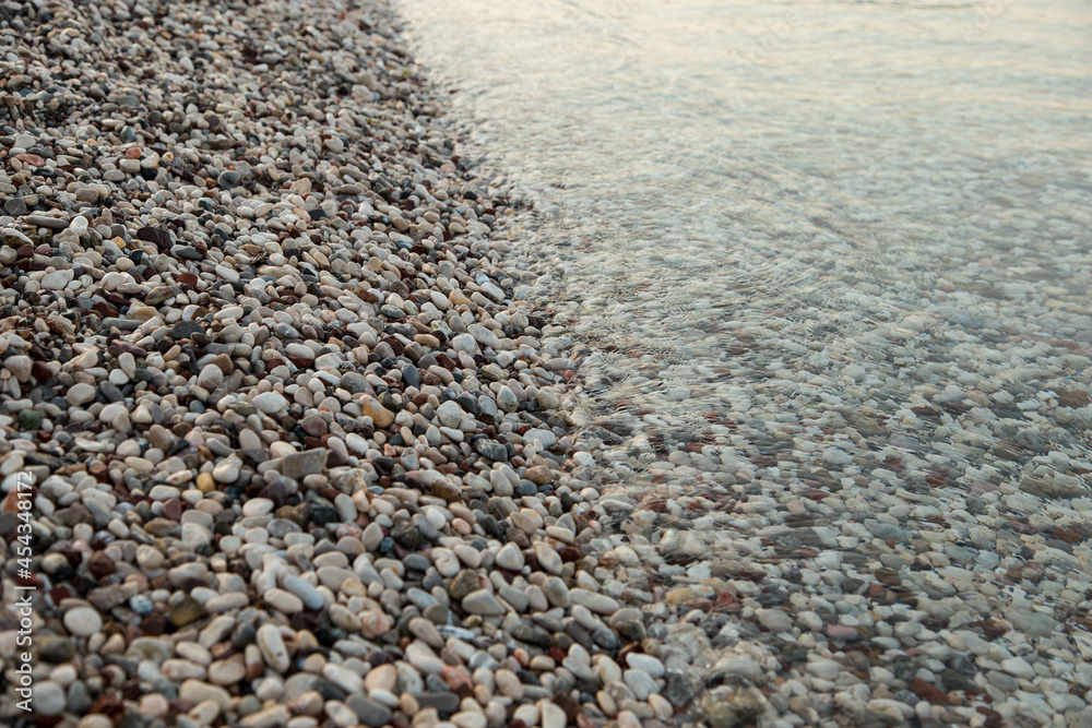 The beach is made of pebbles, the seashore, small colored pebbles in the water. Background, copy space. The beach is made of pebbles, the seashore, small colored pebbles in the water. Background, copy space.