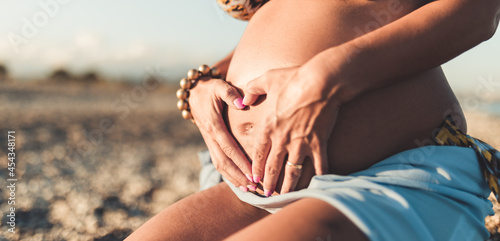 Close up of pregnant girl baby bump. Hands in the shape of a heart on the belly.