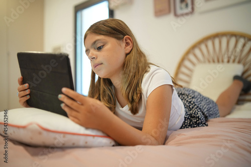 young girl with her tablet watching a video film in her bedroom © goodluz