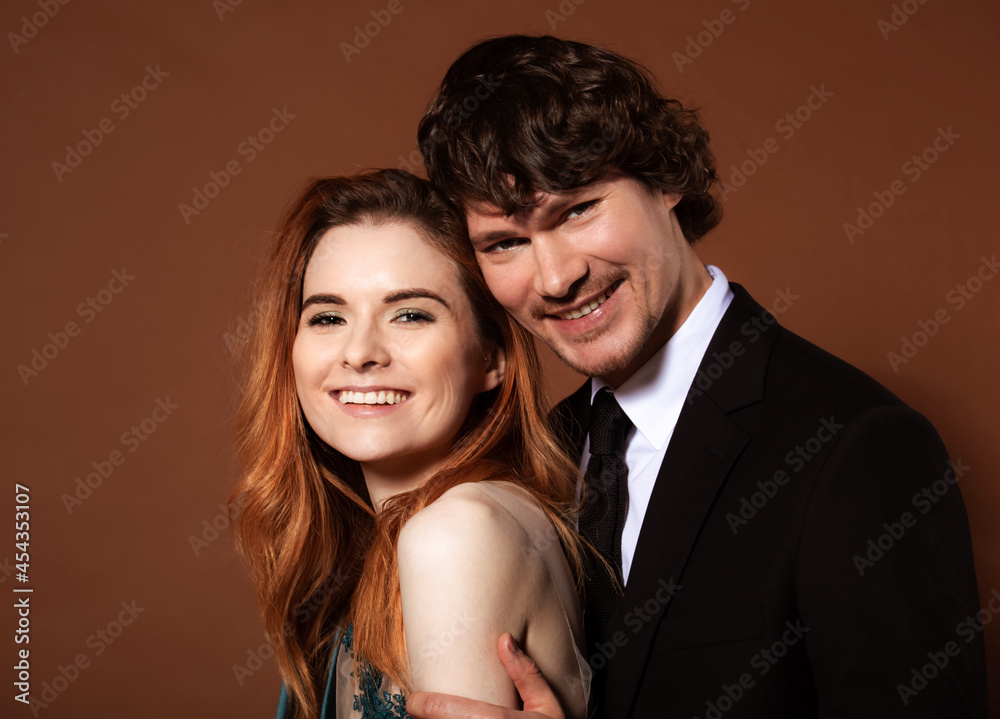 Beautiful red long hair style woman and handsome man with joyful smile celebrating new year holiday on orange bright background. Closeup portrait