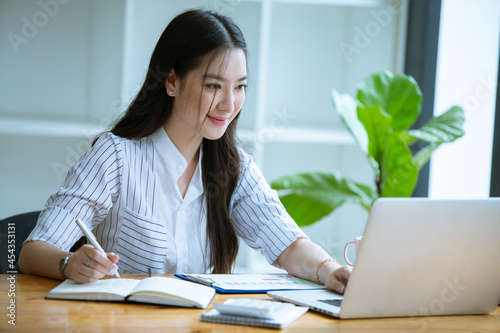 Beautiful Asian woman working freelance working happily Work from home and come up with new projects with her computer, phone and business profit paperwork.