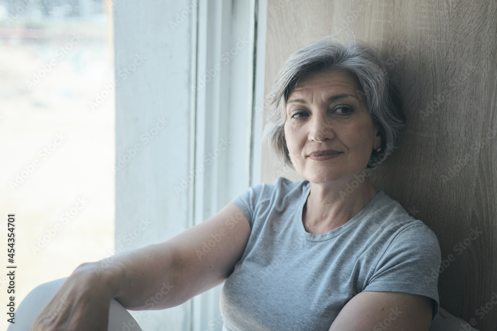 An elderly woman smiling at the window and waiting for her children and grandchildren to return. Happy old age in loneliness and good memories and thoughts of the future. An elderly woman smiling at the window and waiting for her children and grandchildren to return. Happy old age in loneliness and good memories and thoughts of the future.