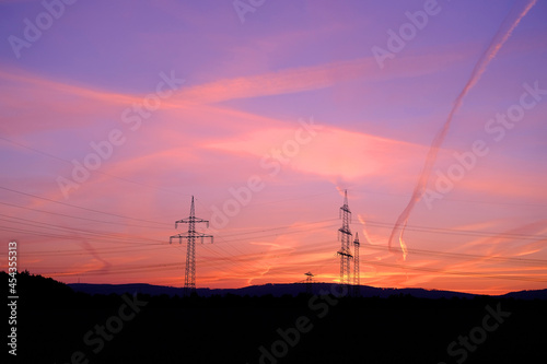 beautiful landscape, sky with airplane trail lines, power towers, field in evening in rays of sunset, concept of beauty of nature, modern energy, technology, bright wallpaper, background for designer