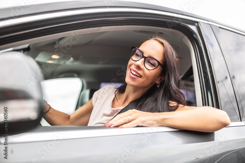 Happy female driver in glasses looks through the open side window of a car she drives © weyo