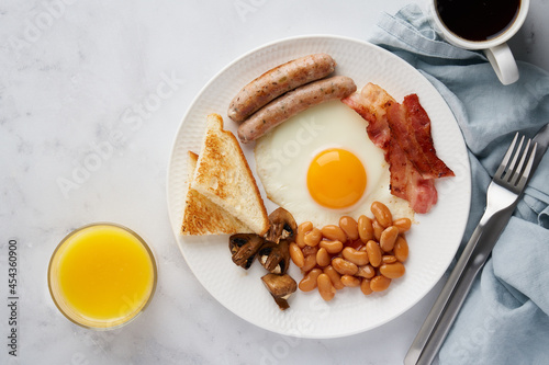 Horizontal top view of typical delicious english cuisine food. English morning breakfast. Mushrooms, egg yolks, bacon, beans, toasts, coffee, orange juice. Light background, copy space