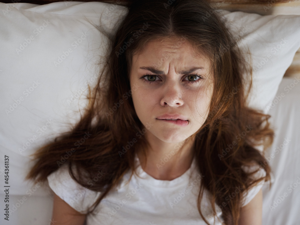 woman with an angry expression bites her lip while lying in bed top view woman with an angry expression bites her lip while lying in bed top view