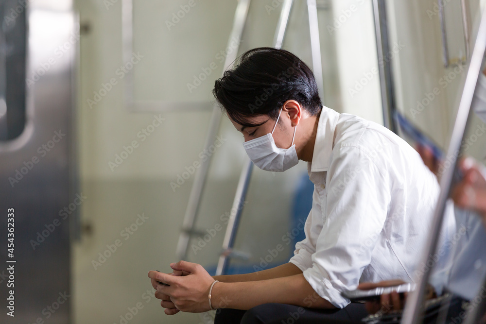 Young Asian businessman sitting and wearing face protective mask for protection from virus disease while using mobile phone on subway train or public transport during coronavirus, or COVID 19 outbreak Young Asian businessman sitting and wearing face protective mask for protection from virus disease while using mobile phone on subway train or public transport during coronavirus, or COVID 19 outbreak