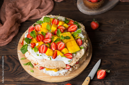 Pavlova with strawberries, mango and coconut cream. Cakes made of cane sugar. Tropical cake. Exotic dessert with mint. Strawberries on a wooden table. New Zealand food