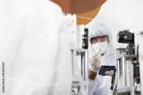 male engineers wearing personal protective equipment uniform(PPE) and medical face mask, checking machine in laboratory