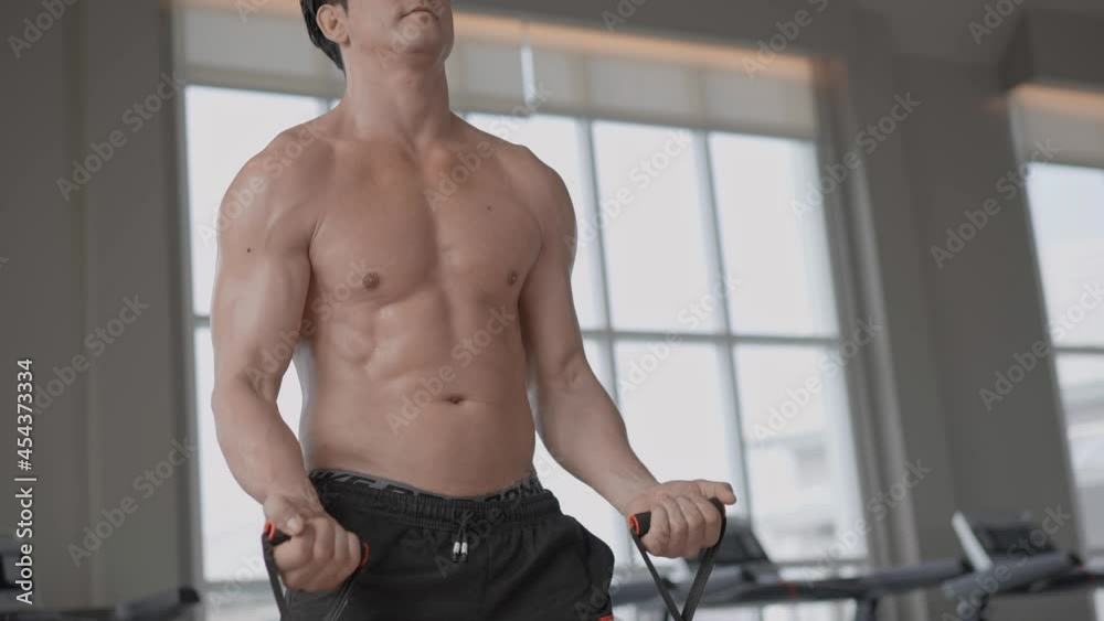 Athletic muscular topless man training with elastic band or resistance rope in the fitness. Strength workout for bodybuilding, chest and biceps. 4K slow motion Athletic muscular topless man training with elastic band or resistance rope in the fitness. Strength workout for bodybuilding, chest and biceps. 4K slow motion