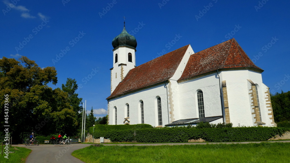 Fototapeta premium sehr schöne Dorfkirche in Poltringen auf grüner Wiese mit Bäumen unter blauem Himmel und Radfahrern